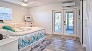 Une chambre avec un lit, un ventilateur de plafond, une télévision et une porte-fenêtre coulissante donnant sur un espace extérieur.