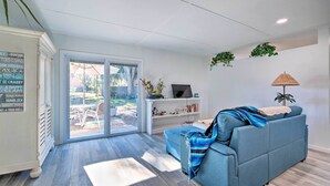 Un salon moderne avec un canapé bleu, un téléviseur posé sur un meuble blanc, une bibliothèque et une grande porte-fenêtre coulissante donnant sur un espace extérieur.