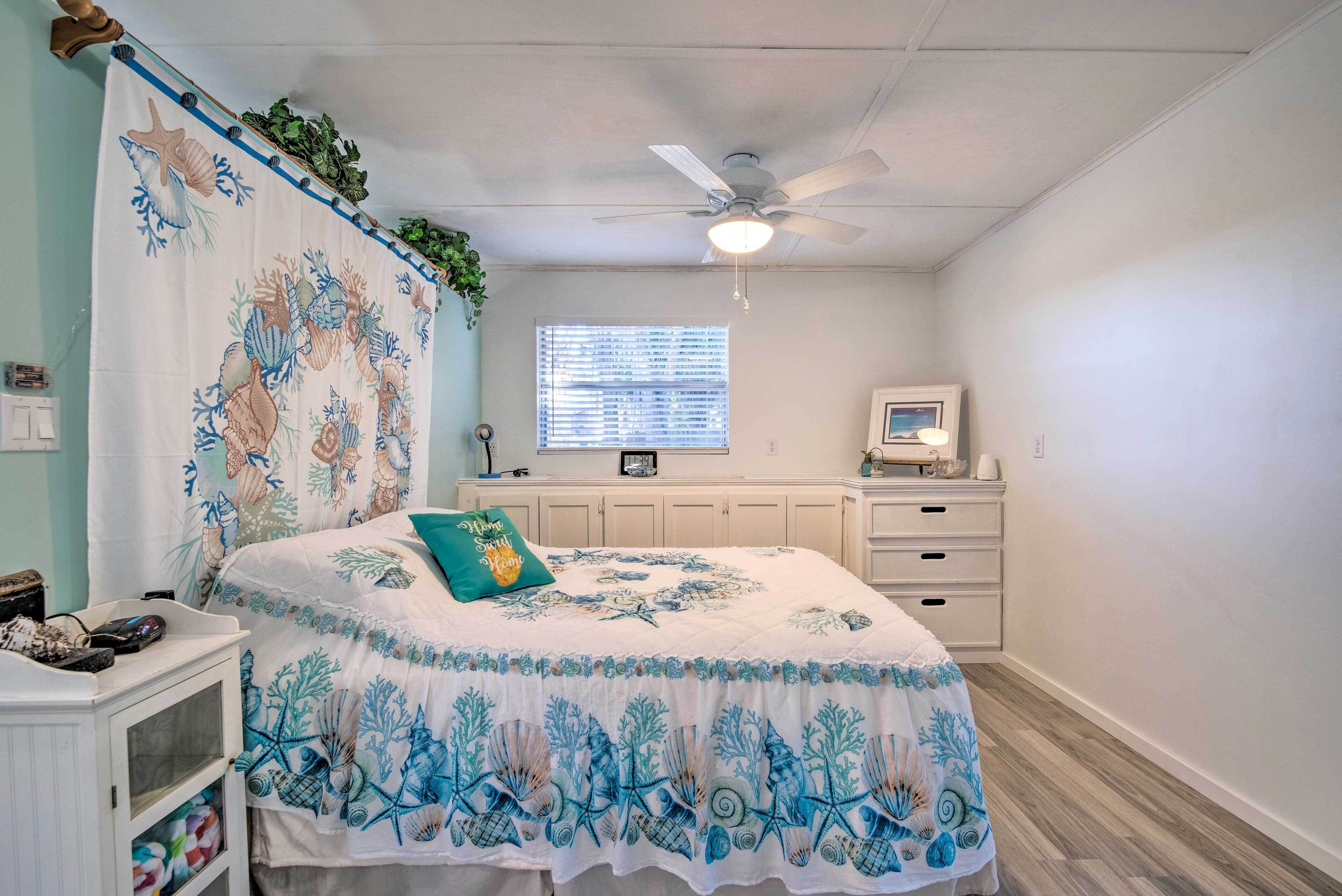 A bedroom with a bed, a ceiling fan, a window, a desk, and a dresser.