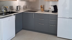 Una cocina moderna con gabinetes grises, una campana extractora de acero inoxidable, lavavajillas integrado y un refrigerador.