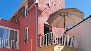 Un edificio de dos pisos con un balcón, una escalera de madera y una puerta.