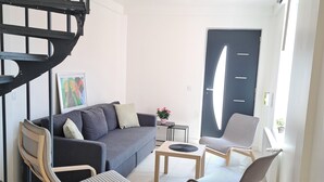 Una sala de estar moderna con un sofá gris, dos sillas de madera, una mesita y una escalera espiral negra.