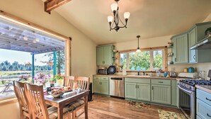 A kitchen with wooden flooring, green cabinets, and a dining area with a table and chairs. - Family Home w/ Stunning River & Mountain View (Priest River)
