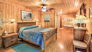 A wooden cabin bedroom with a bed, nightstand, lamp, and a small desk with a chair. - Family Home w/ Stunning River & Mountain View (Priest River)