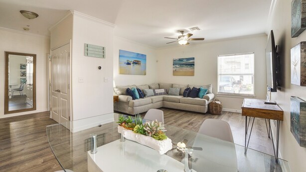 A modern living room with a glass coffee table, a grey sectional sofa, and a ceiling fan.