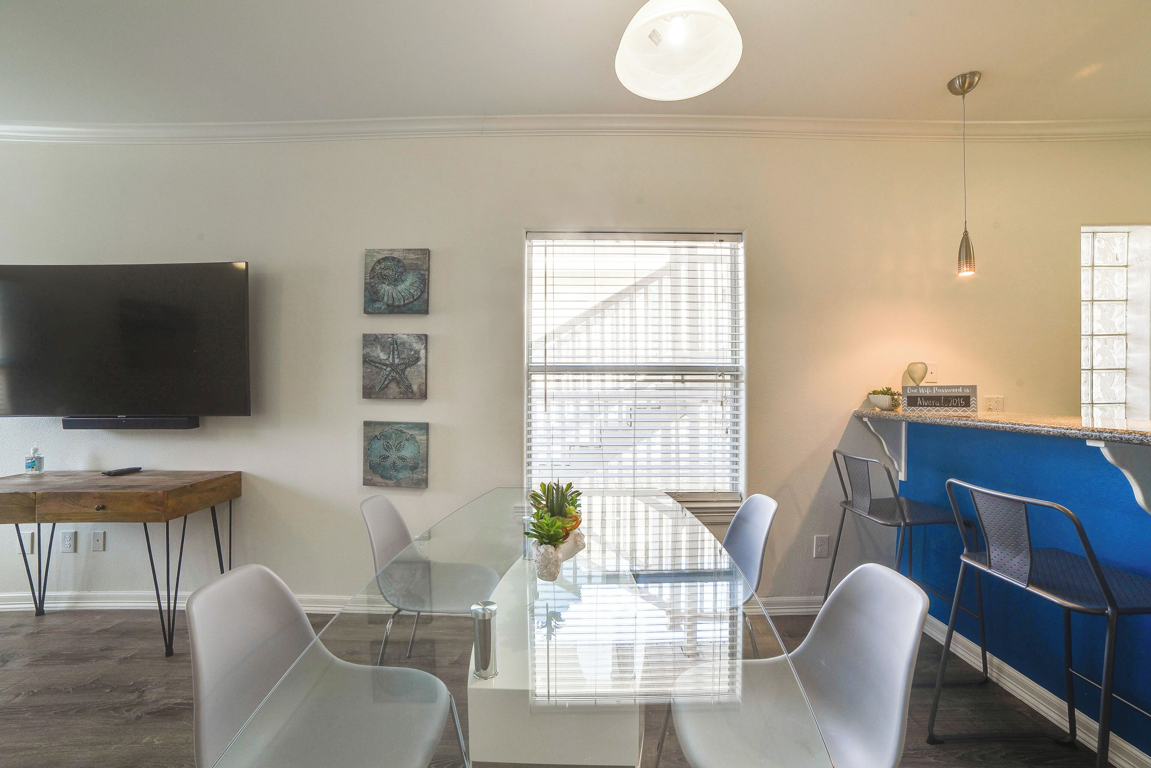 A modern kitchen with a blue countertop, a glass dining table, and a TV mounted on the wall.