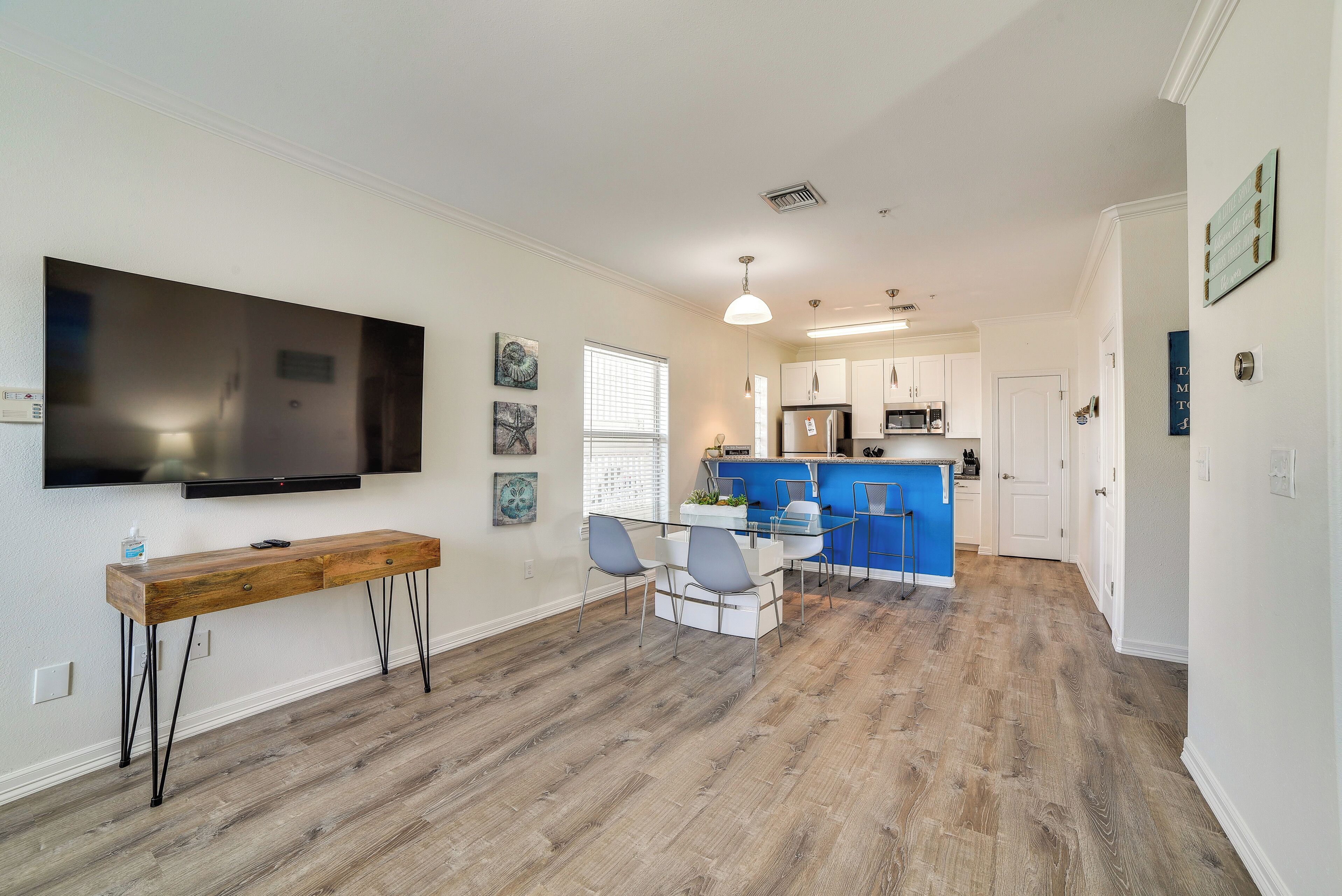 A modern kitchen with a blue island, a dining area with a wooden table and chairs, and a large flat-screen TV mounted on the wall.