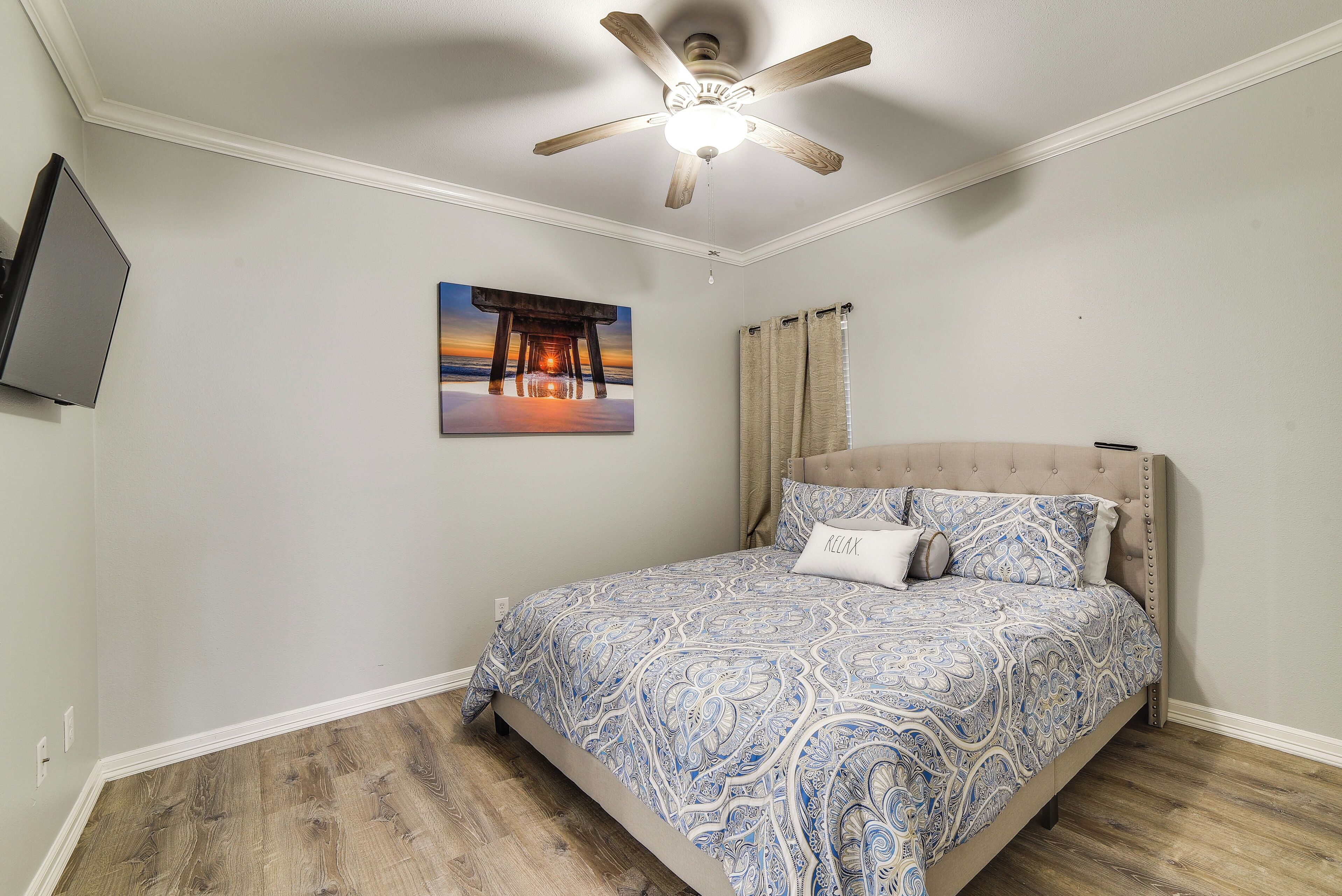 A bedroom with a bed, a ceiling fan, a wall-mounted TV, and a painting.
