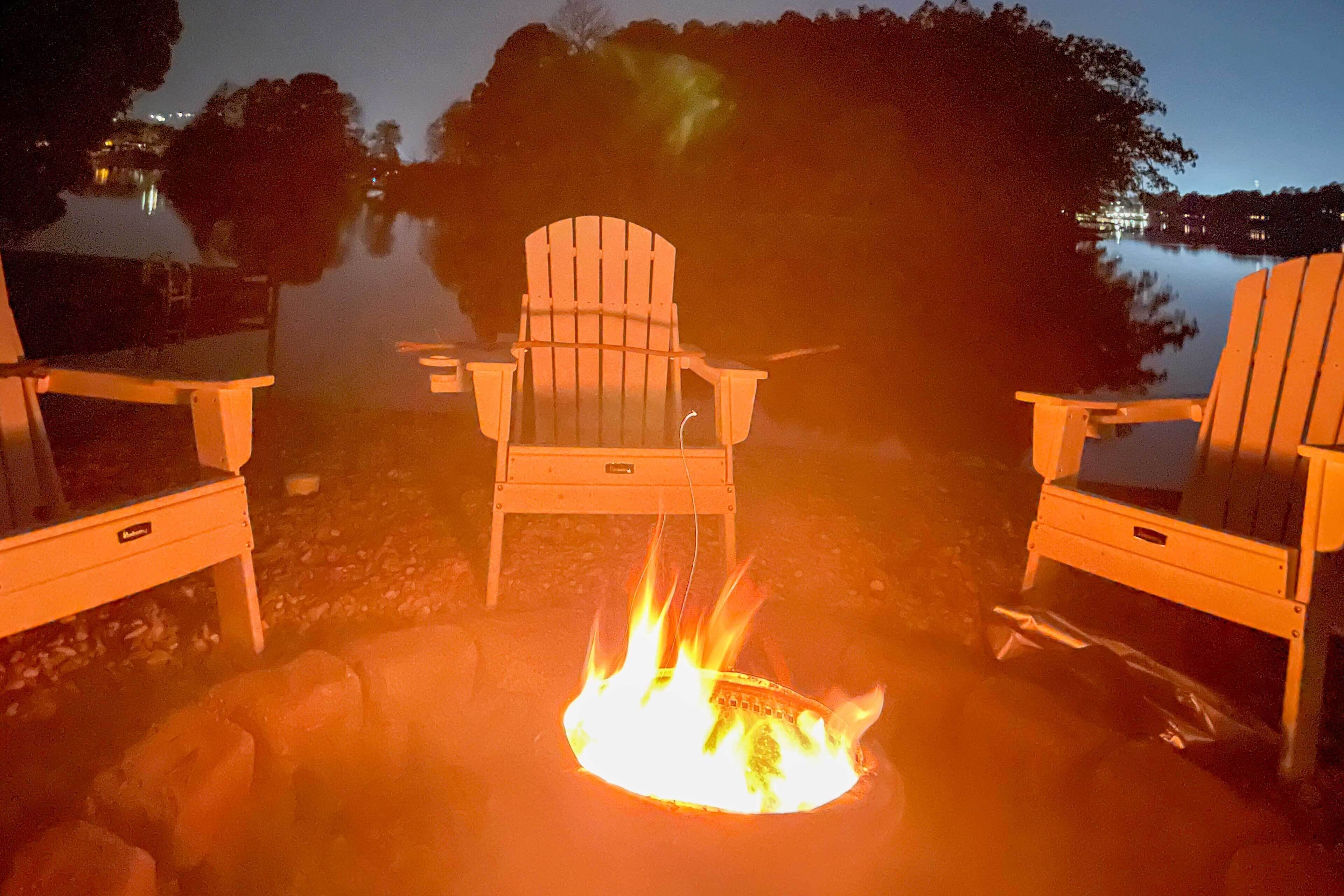 Un hogar con dos sillas Adirondack a su alrededor, con un lago tranquilo y árboles como fondo.