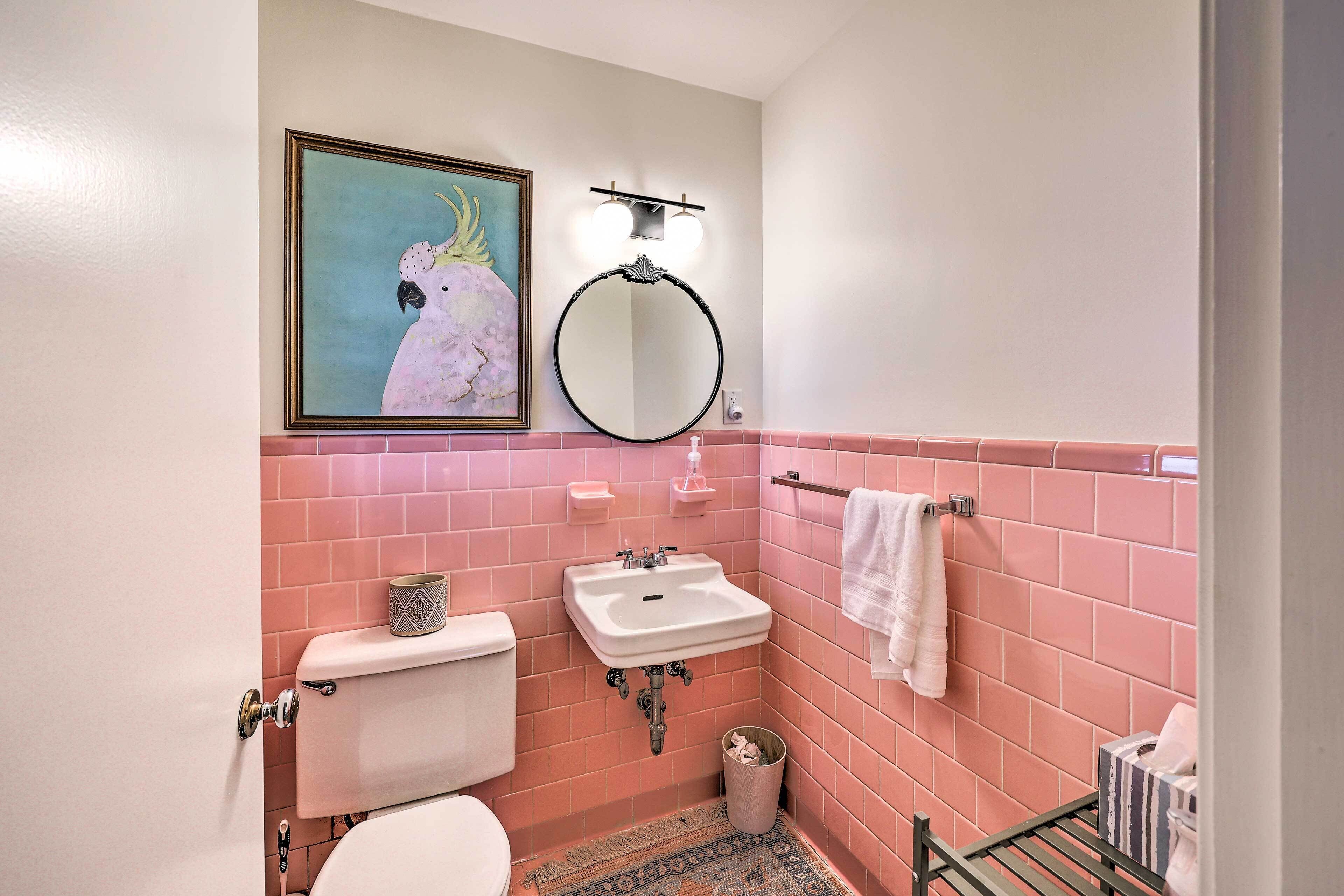 Une salle de bain avec des carreaux roses, des toilettes, un lavabo, un miroir et un tableau encadré représentant un oiseau.
