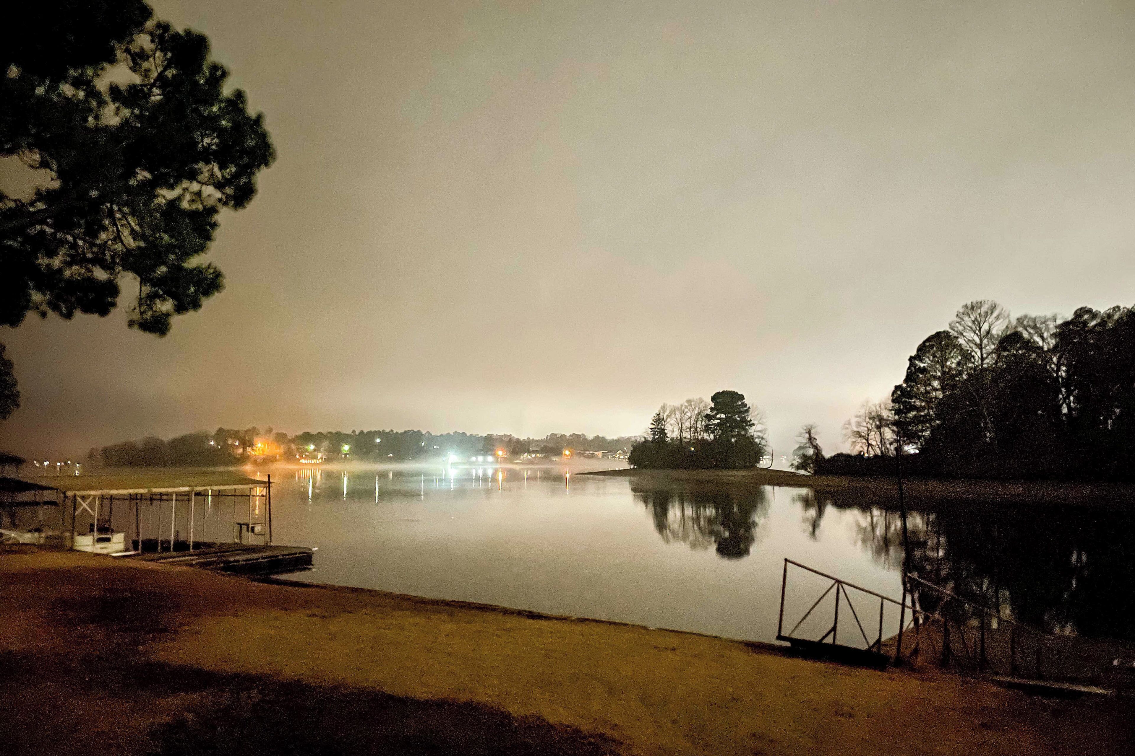 A calm lake at night with a dock and a covered seating area.
