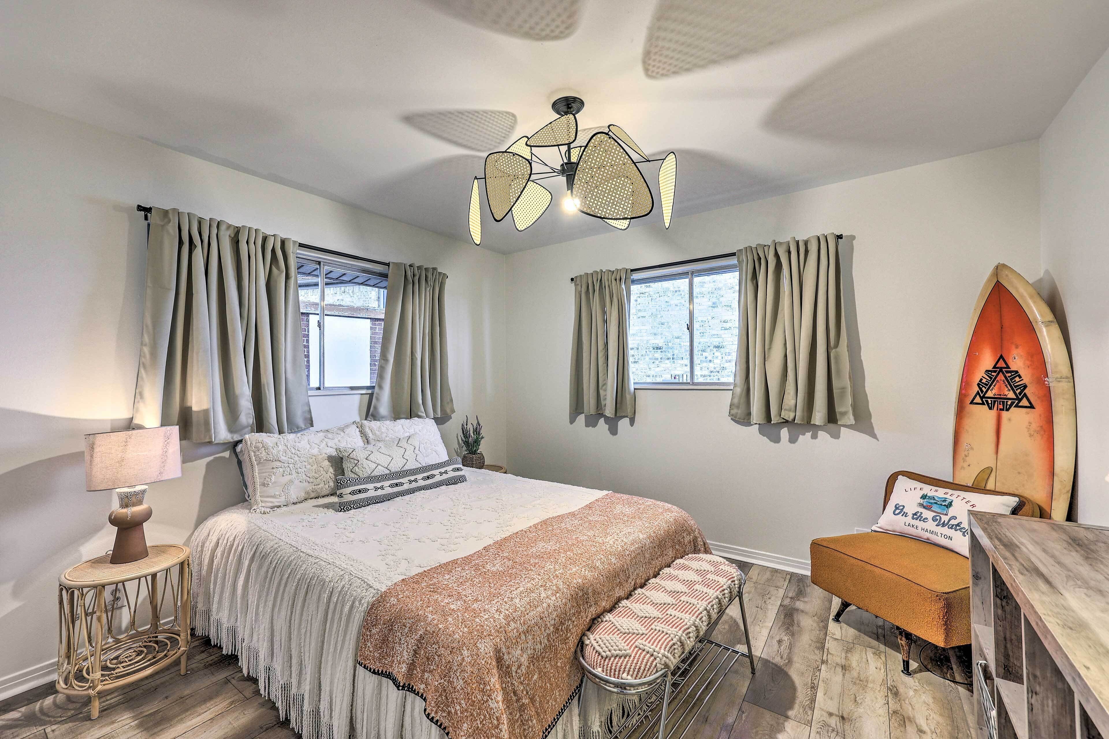 Une chambre à coucher avec un lit, une table de chevet avec une lampe, une chaise, une planche de surf et un ventilateur de plafond.