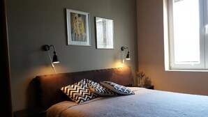 Un letto rifatto con cuscini a fantasia, due lampade a parete e opere d'arte incorniciate sopra.