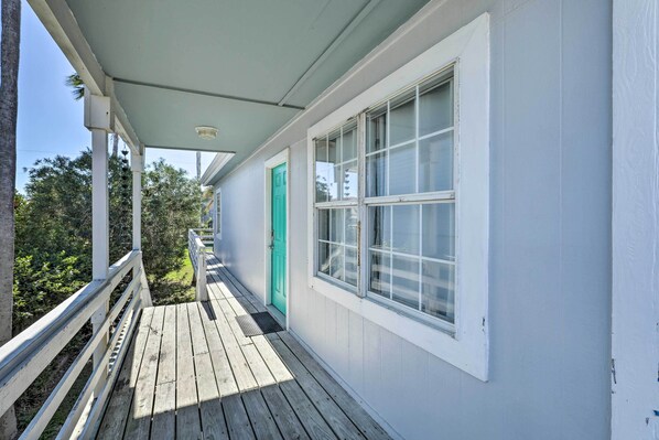 A covered wooden deck with a white railing, a green door, and a window with white trim.