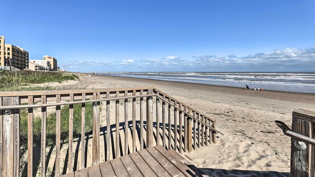 En träpromenad som leder till en sandstrand med en klar himmel.