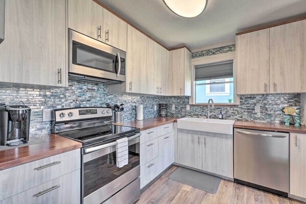 A modern kitchen with stainless steel appliances, light wood cabinetry, and a blue-tiled backsplash.