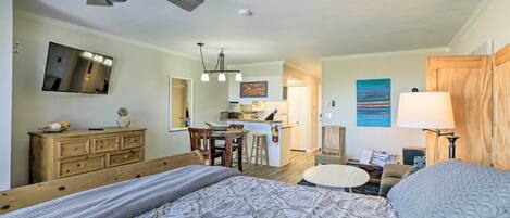 A bedroom with a bed, wooden dresser, and a kitchenette in the background.