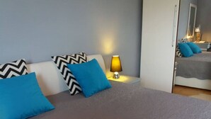A neatly made bed with a grey bedspread and two blue pillows, a bedside lamp, and a mirror reflecting part of the room. - Apartments Villa Dona - Superior Double Room (Vela Luka)