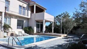 Een huis met twee verdiepingen, een zwembad, terrasmeubels en een pergola.