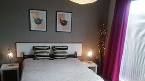 Een slaapkamer met een groot bed, twee nachtkastjes, een hanglamp en een raam met gordijnen.