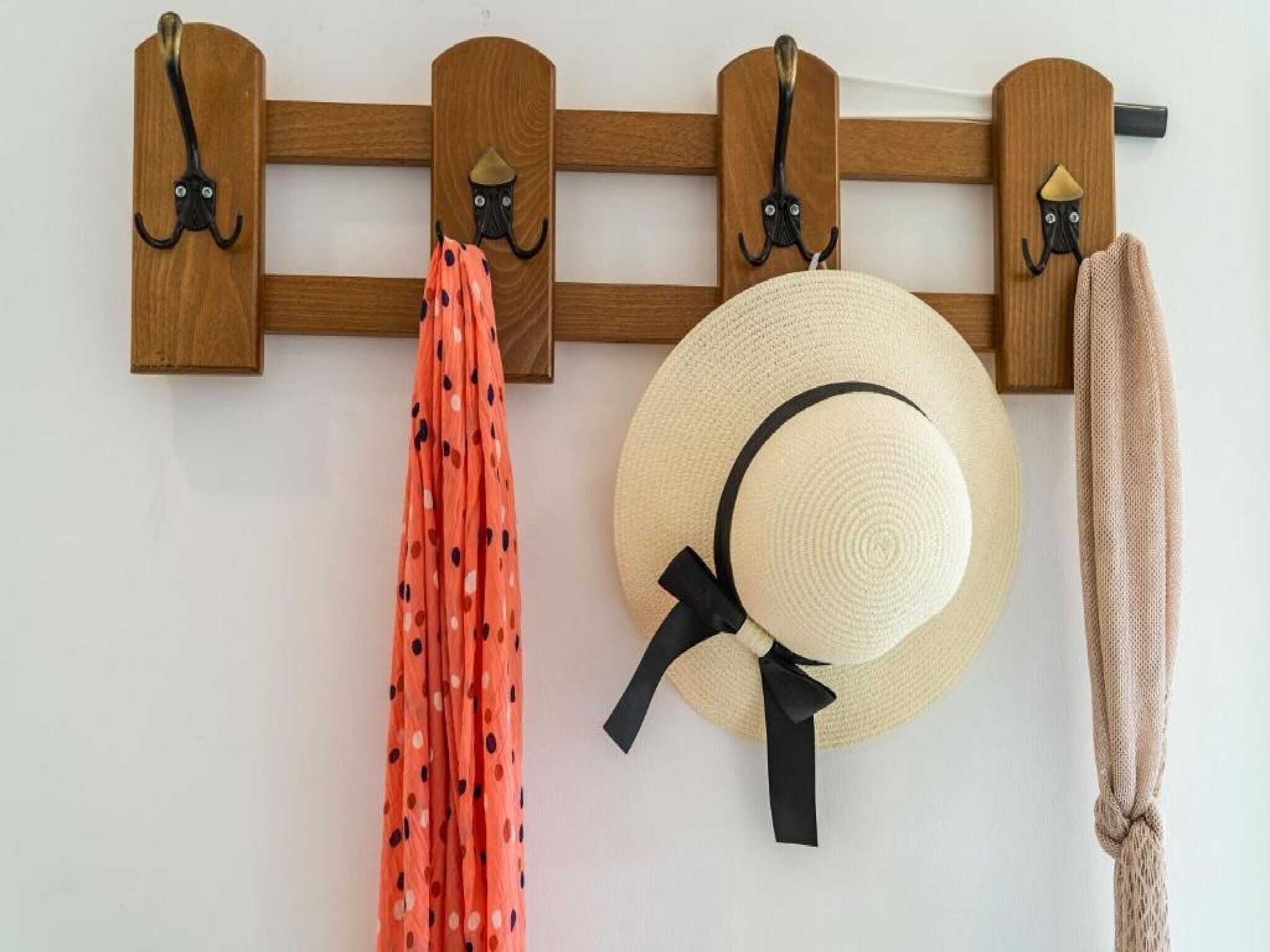 A wall-mounted coat rack with three hooks, each holding a hat and a scarf.