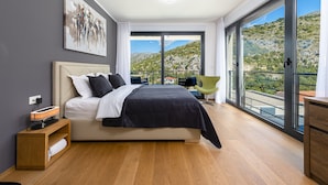 A modern bedroom with a large bed, a bedside table, a chair, and a balcony with a scenic view.