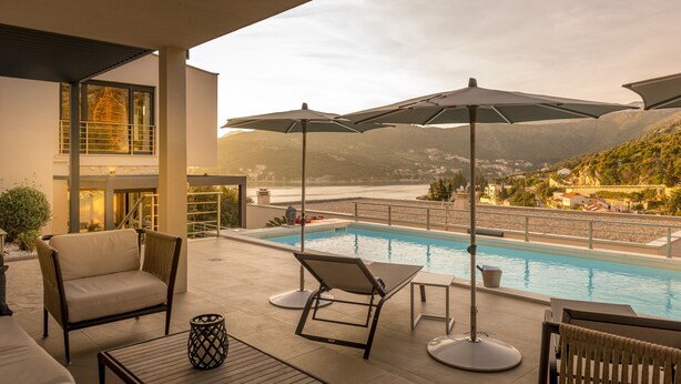 A poolside area with lounge chairs, umbrellas, and a view of a lake and mountains.