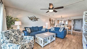 A living room with a ceiling fan, two sofas, a coffee table, and a kitchen area in the background. - Beachfront PCB Escape w/ Free Beach Chair Services (Panama City Beach)