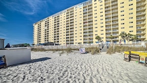A large hotel with multiple floors and balconies, situated on a sandy beach with palm trees and a clear blue sky. - Beachfront PCB Escape w/ Free Beach Chair Services (Panama City Beach)