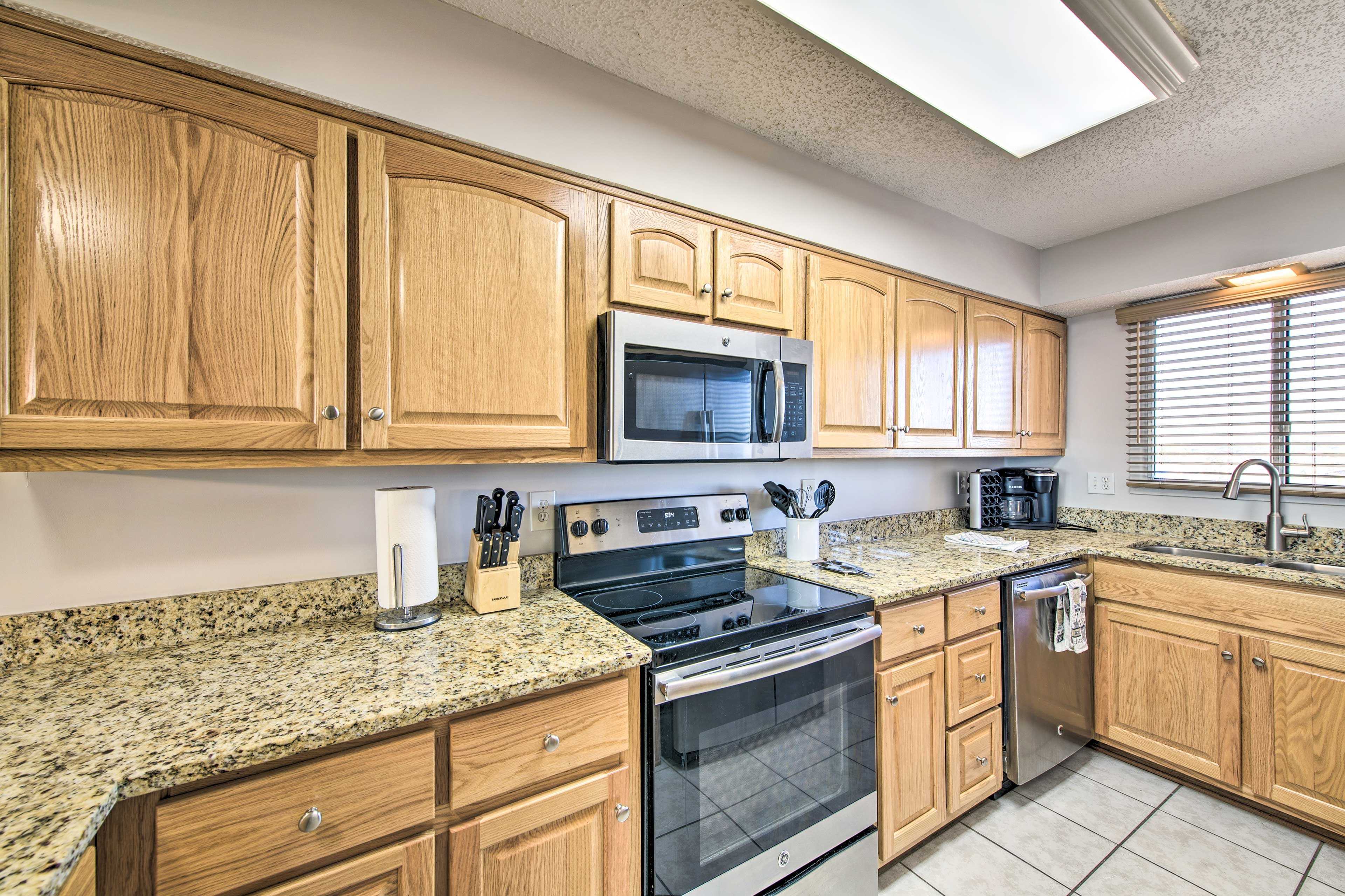 A kitchen with wooden cabinets, a stainless steel oven, a microwave, granite countertops, and a window with blinds.