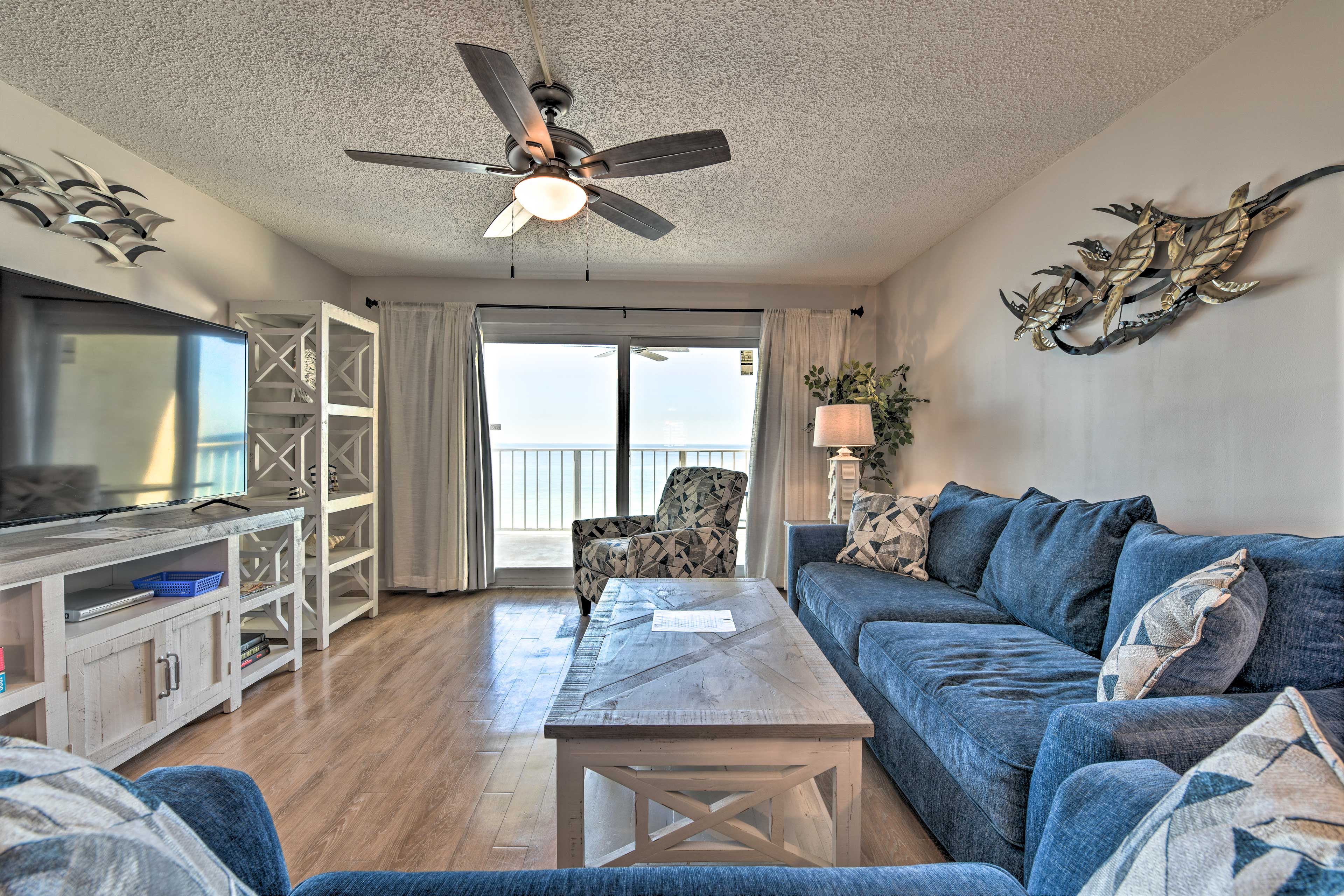 A living room with a ceiling fan, a television, a sofa, a coffee table, and a view through a glass door.