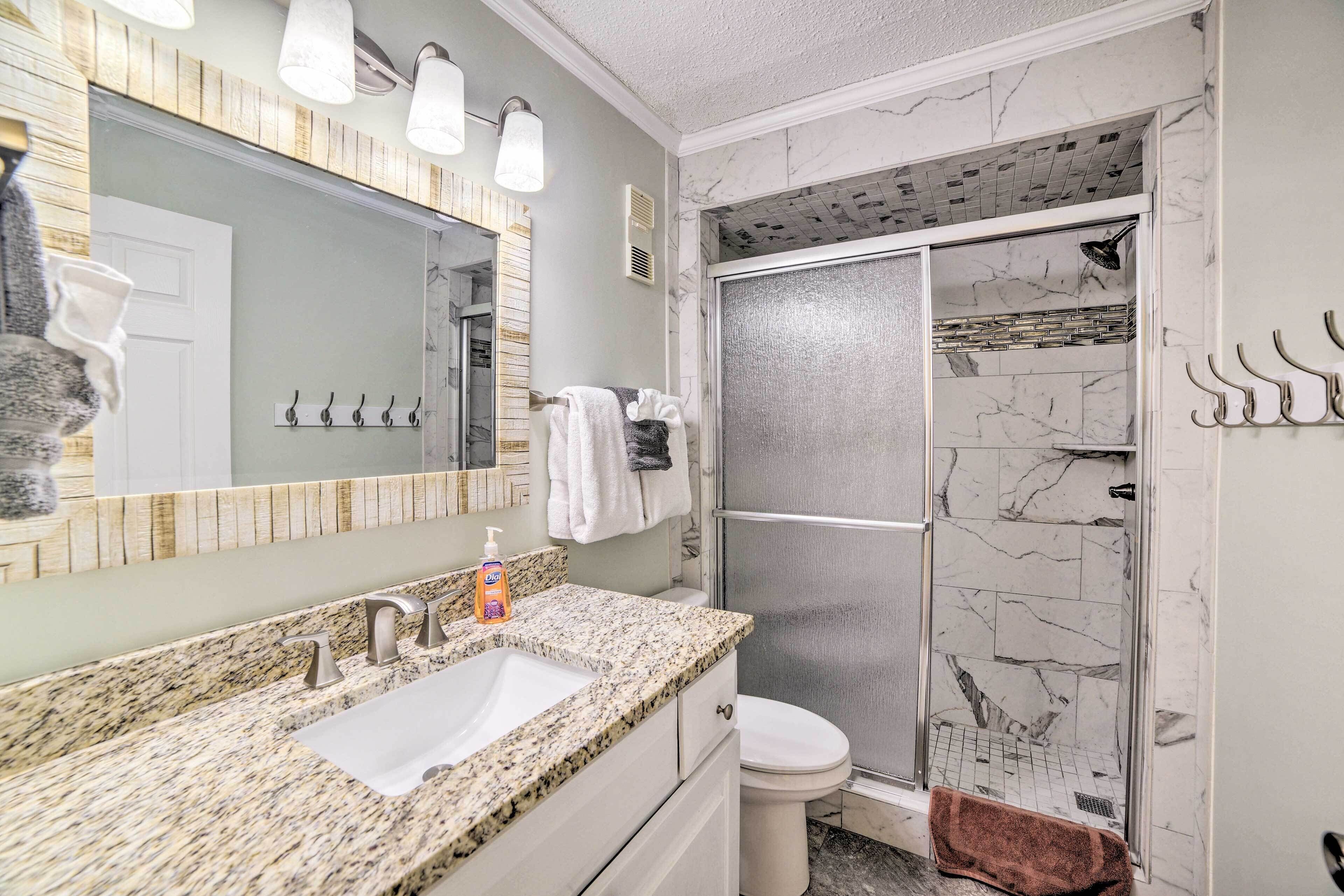 A bathroom with a granite countertop sink, a mirror with a wooden frame, a shower with a glass door, and a marble backsplash.