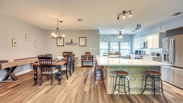 Une cuisine moderne dotée d’un îlot central, de tabourets de bar, d’un plancher en bois et de luminaires suspendus.