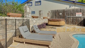Une maison avec un mur en pierre, une clôture en bois et un espace piscine équipé de chaises longues.