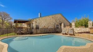 Une maison en pierre avec une piscine, un patio couvert et un mur en pierre.