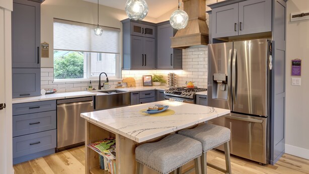 A modern kitchen with grey cabinets, stainless steel appliances, and pendant lighting.