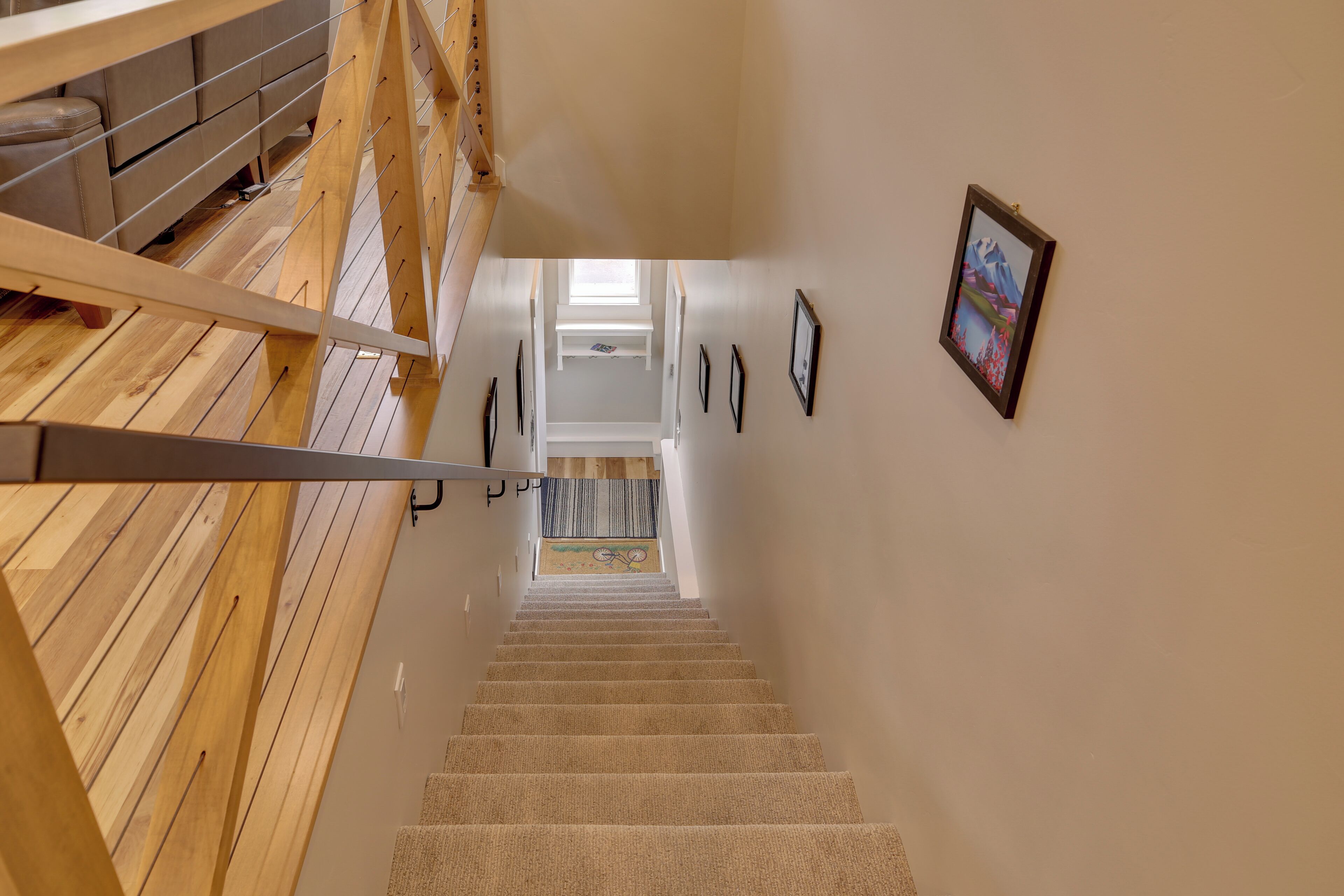 Eine Holztreppe führt zu einer Zwischenebene mit Blick auf einen Raum, der ein Bett und ein Fenster zeigt.