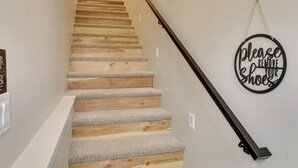 A staircase with wooden steps and carpeted risers, a black handrail, and a sign on the wall that says "Please remove your shoes."