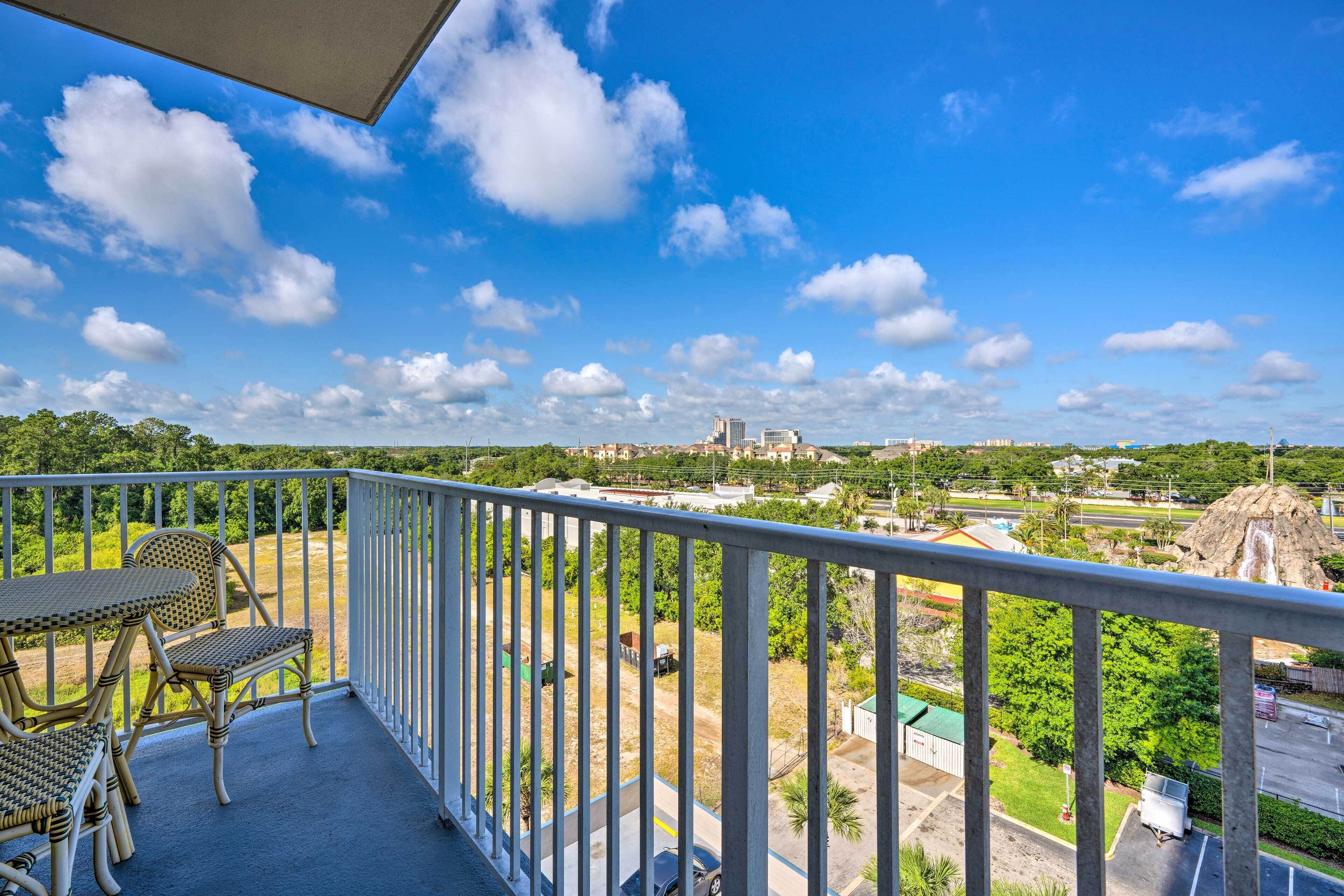A balcony with wicker furniture, a view of a cityscape, and a clear blue sky.
