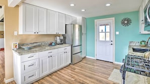 Una cocina con armarios blancos, un refrigerador de acero inoxidable, una estufa a gas y una pared de acento color aguamarina.