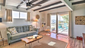 Sala de estar con sofá, mesa de centro y ventilador de techo. Se ve el exterior a través de un ventanal.