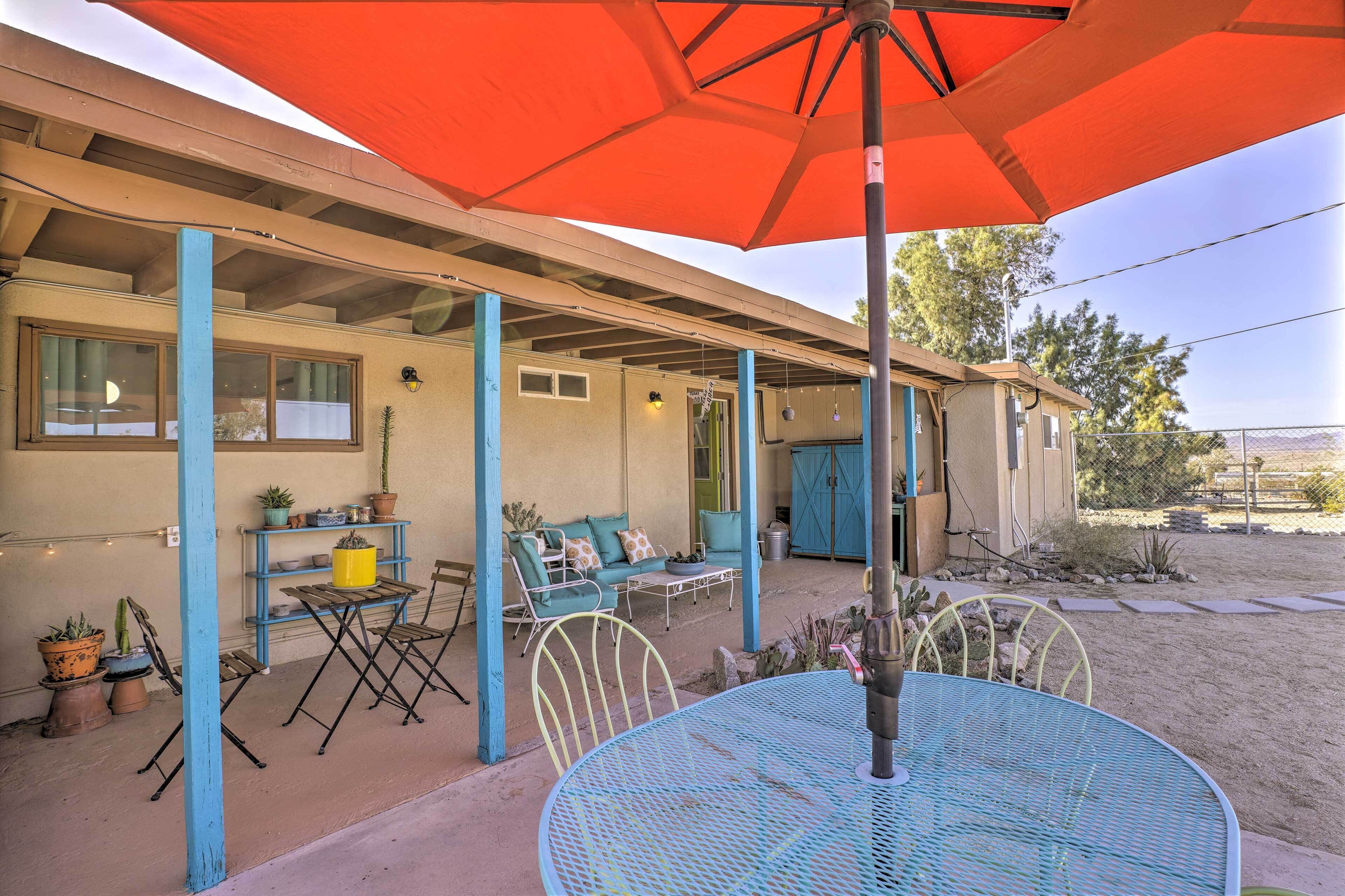 An outdoor patio with a blue metal table and chairs, a red umbrella, and potted plants.