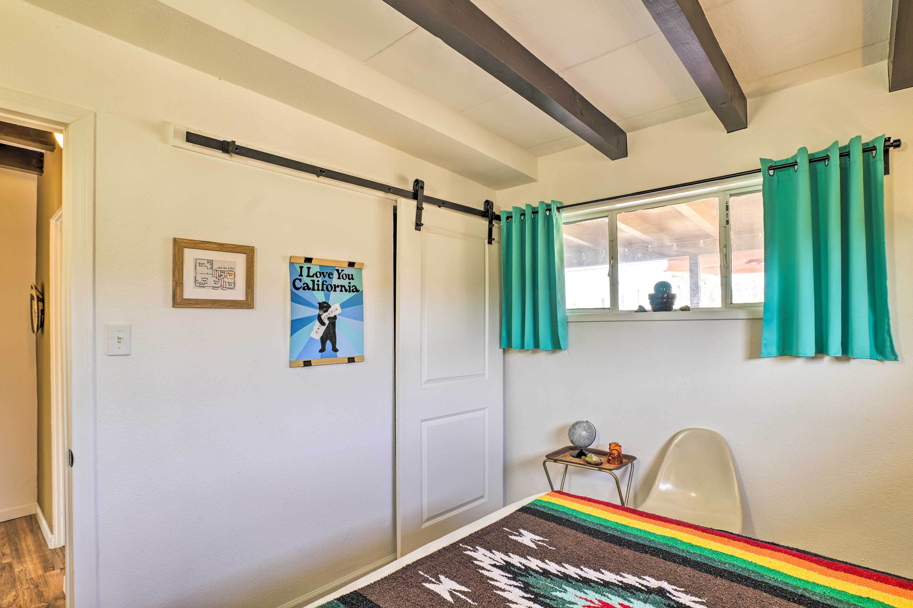 A room with a bed, a window with curtains, a small table with a globe, and a poster on the wall.