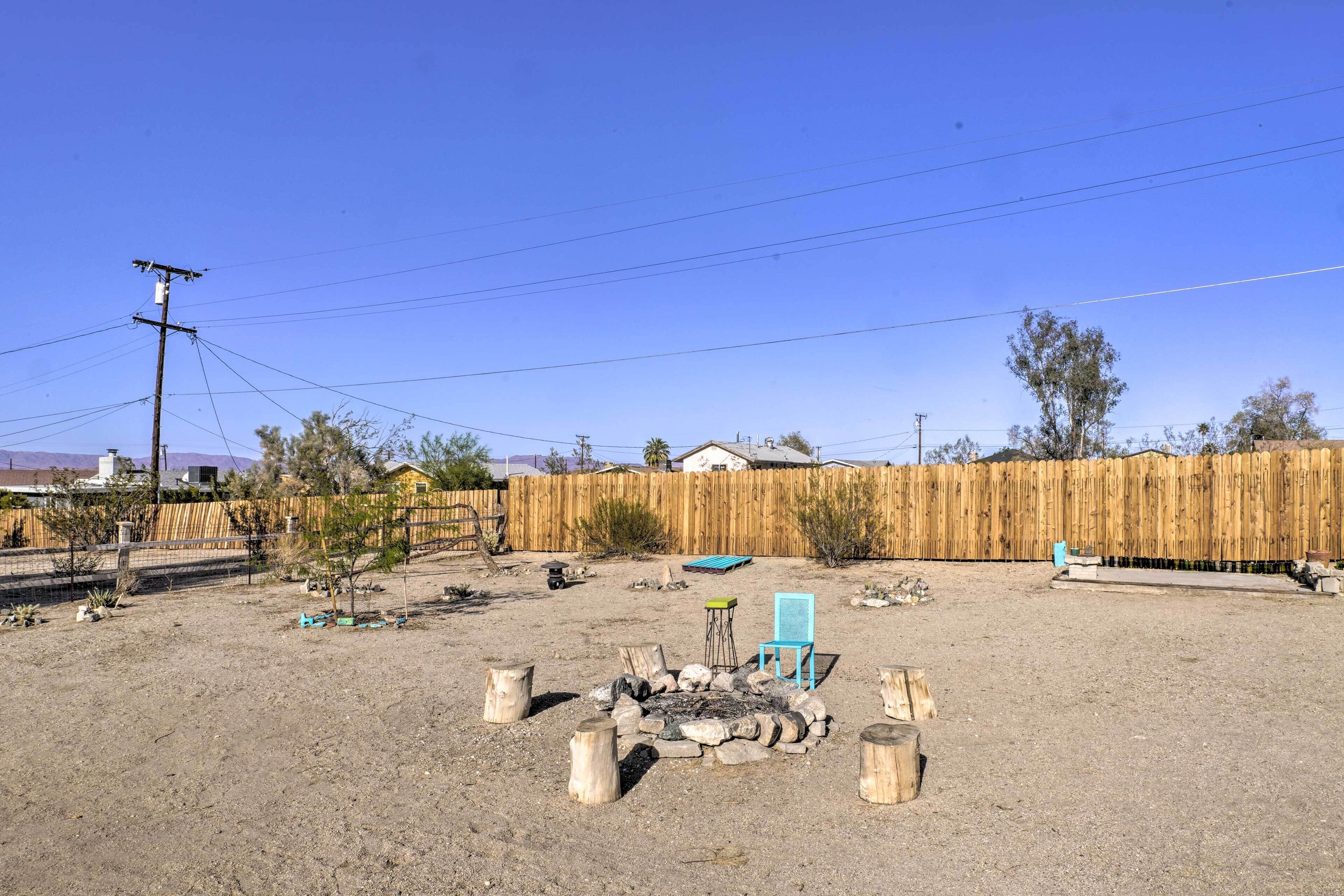Un espacio al aire libre con una fogata, asientos de madera y una silla azul.