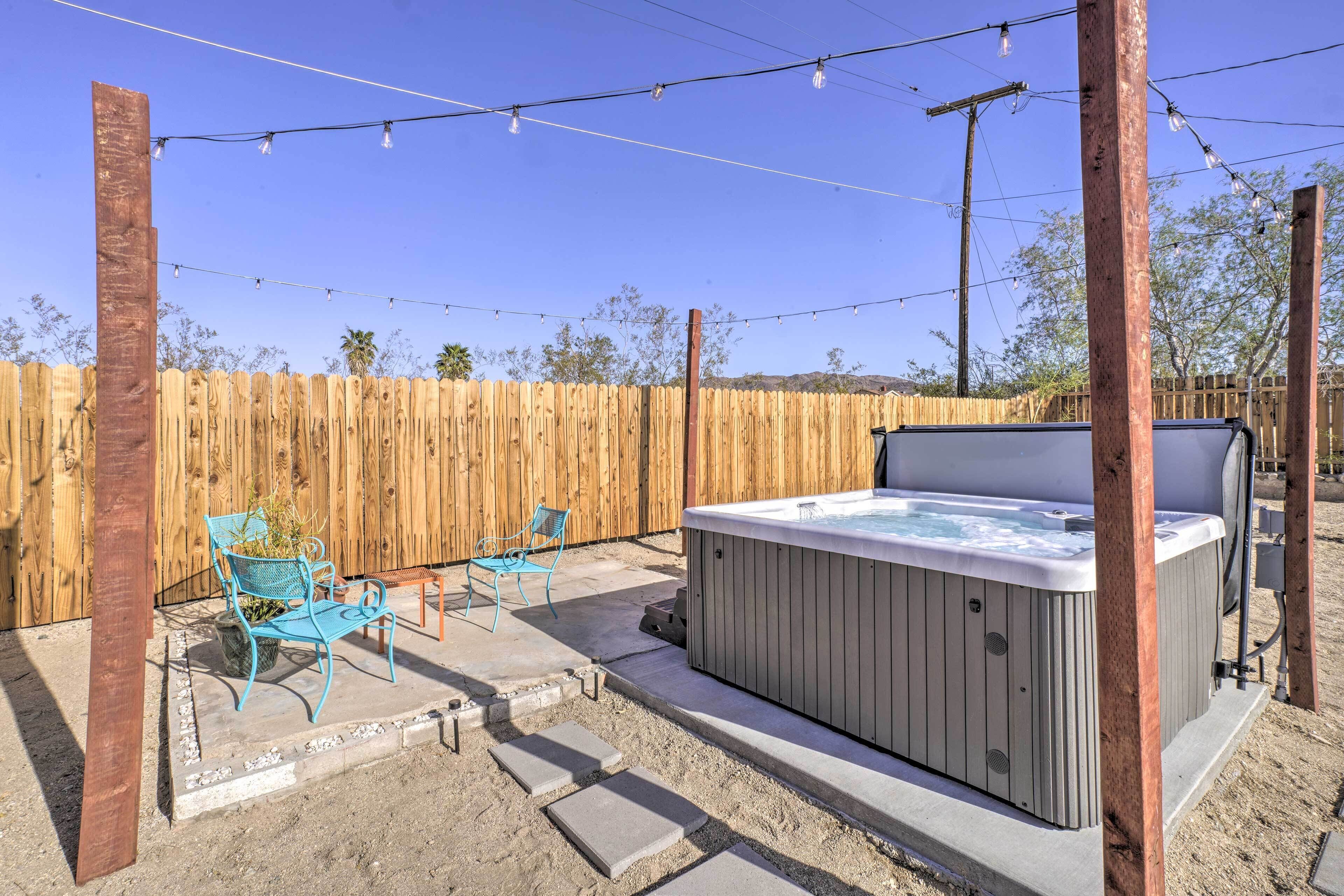 A backyard with a hot tub, outdoor furniture, and string lights.