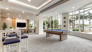 A modern lounge area with a pool table, bar stools, a television, and large windows offering a view of palm trees and buildings. - Modern Ft Lauderdale Condo ~ 7 Mi to Airport! (Fort Lauderdale)