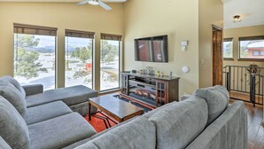 A living room with a fireplace, large windows, and a ceiling fan. - Pagosa Springs Vacation Rental w/ Boat Dock! (Pagosa Springs)