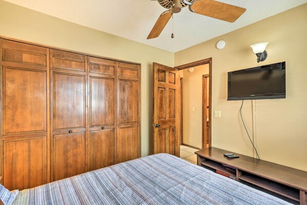 Un dormitorio con cama, armario de madera, ventilador de techo, televisor y l ámpara.