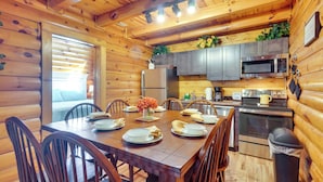 L’intérieur d’un chalet en bois comprend une table à manger pour quatre personnes, des appareils de cuisine et une poubelle.