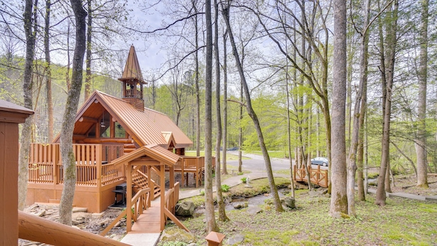 Une cabane en bois dotée d’un clocher, entourée d’arbres et bordée d’un petit ruisseau.